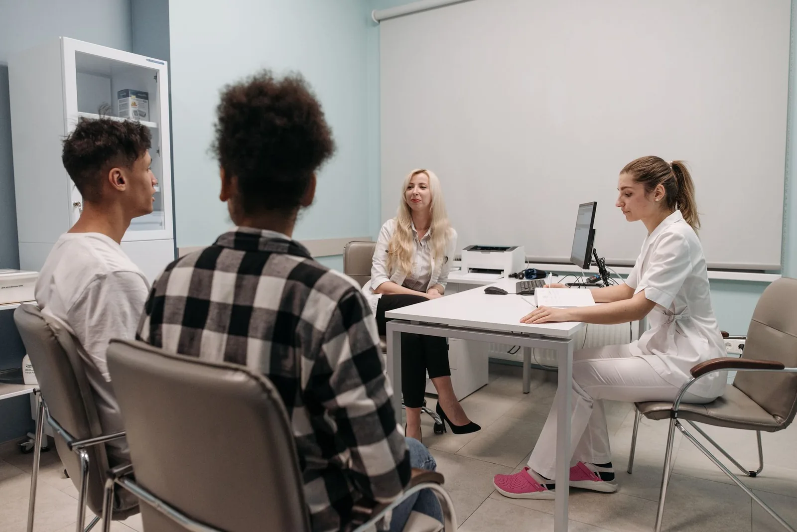A patient and a companion seated across a desk from a doctor, talking through treatment options in a clinic office.
