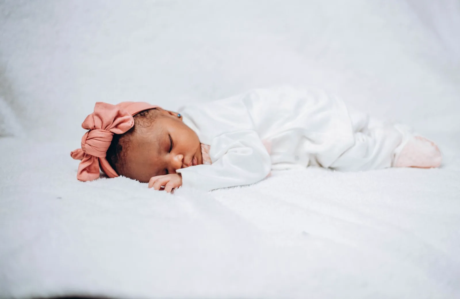 A baby sleeping peacefully, settled on soft white fabric.