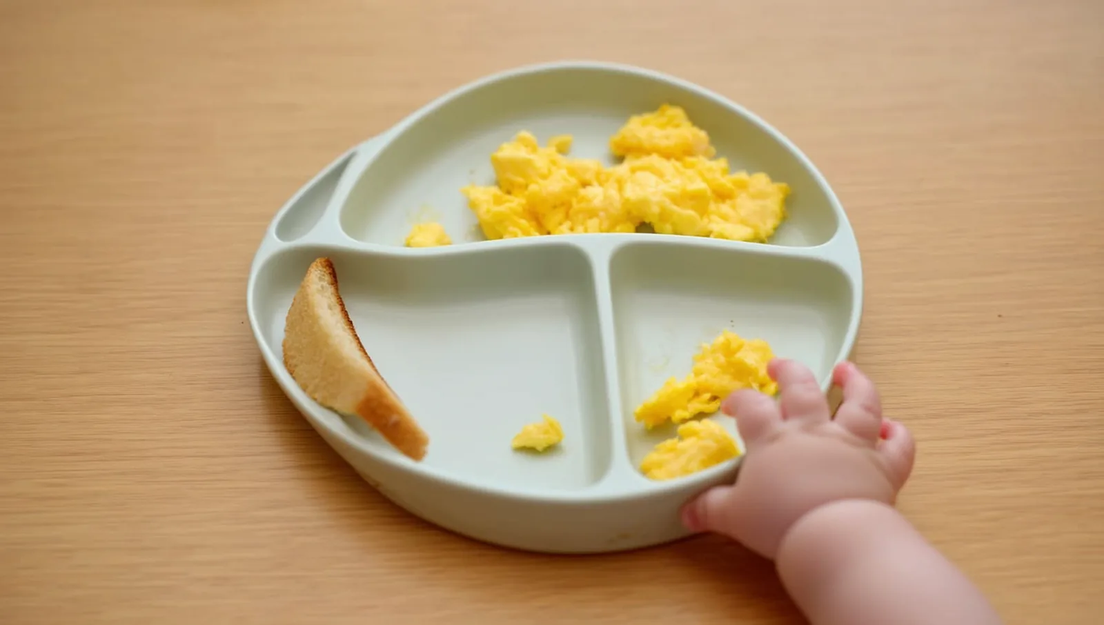Baby hand reaching for scrambled egg on a plate