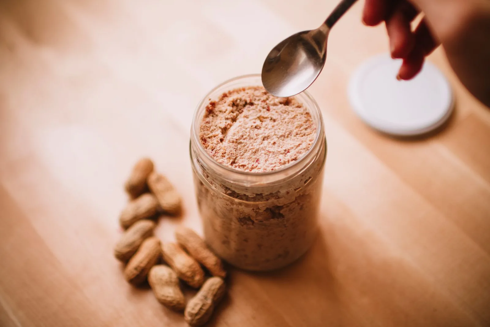 Glass jar of peanut butter with peanuts and a spoon