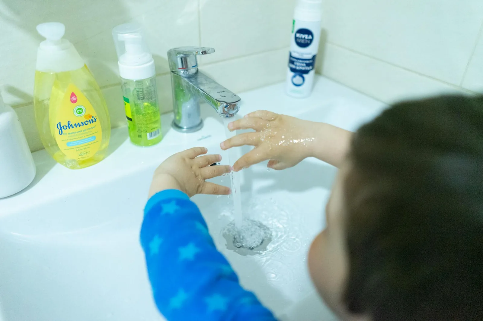 Child washing hands with soap under running water, a daily trigger for pediatric hand eczema.